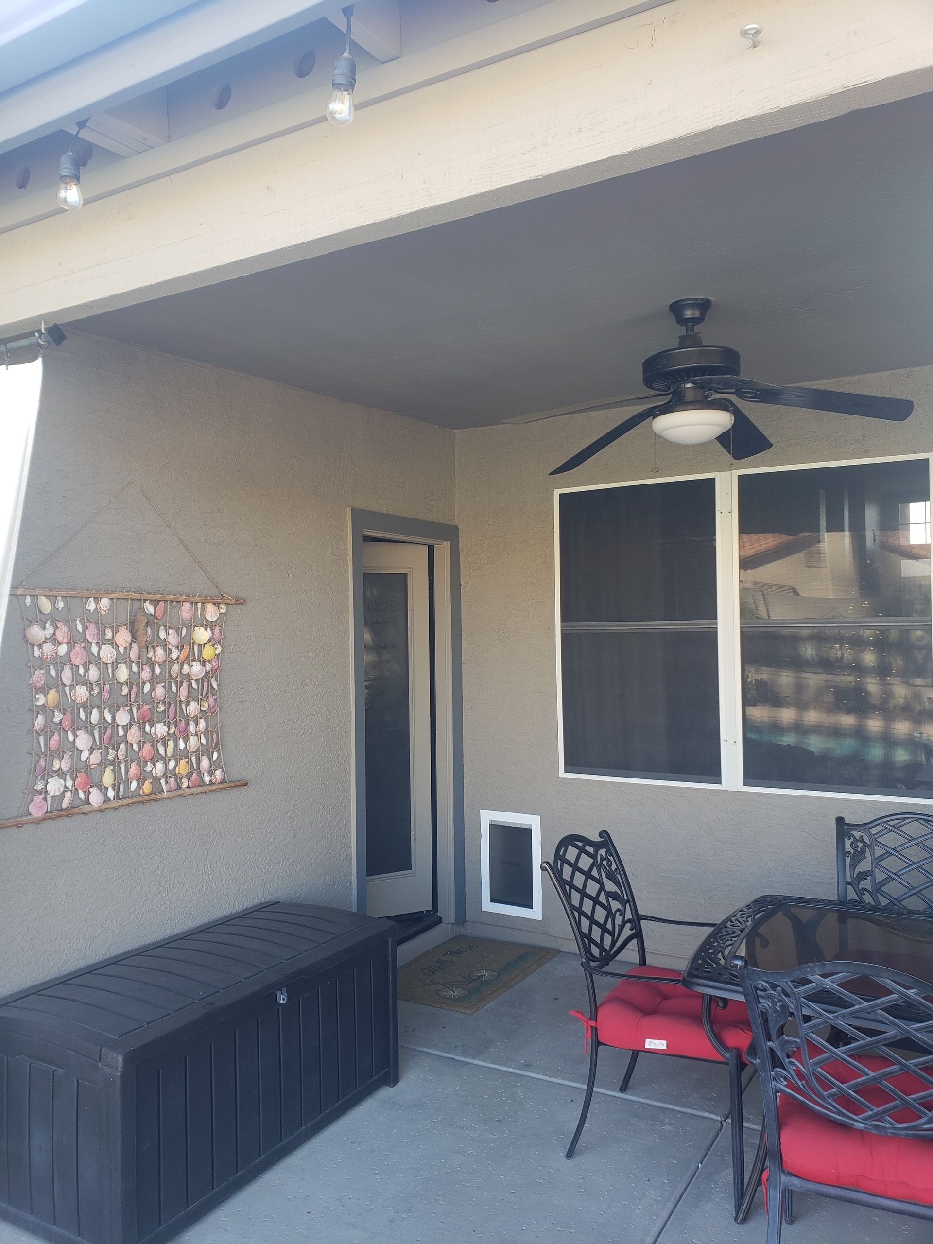 Covered patio with a black storage chest, table, chairs, and a ceiling fan.