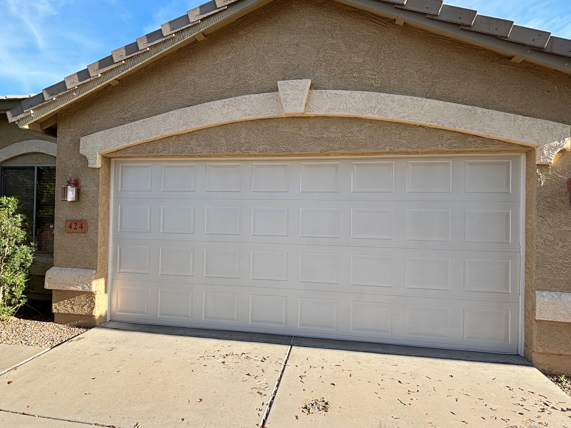 White garage door on a tan house with a concrete driveway under a blue sky.