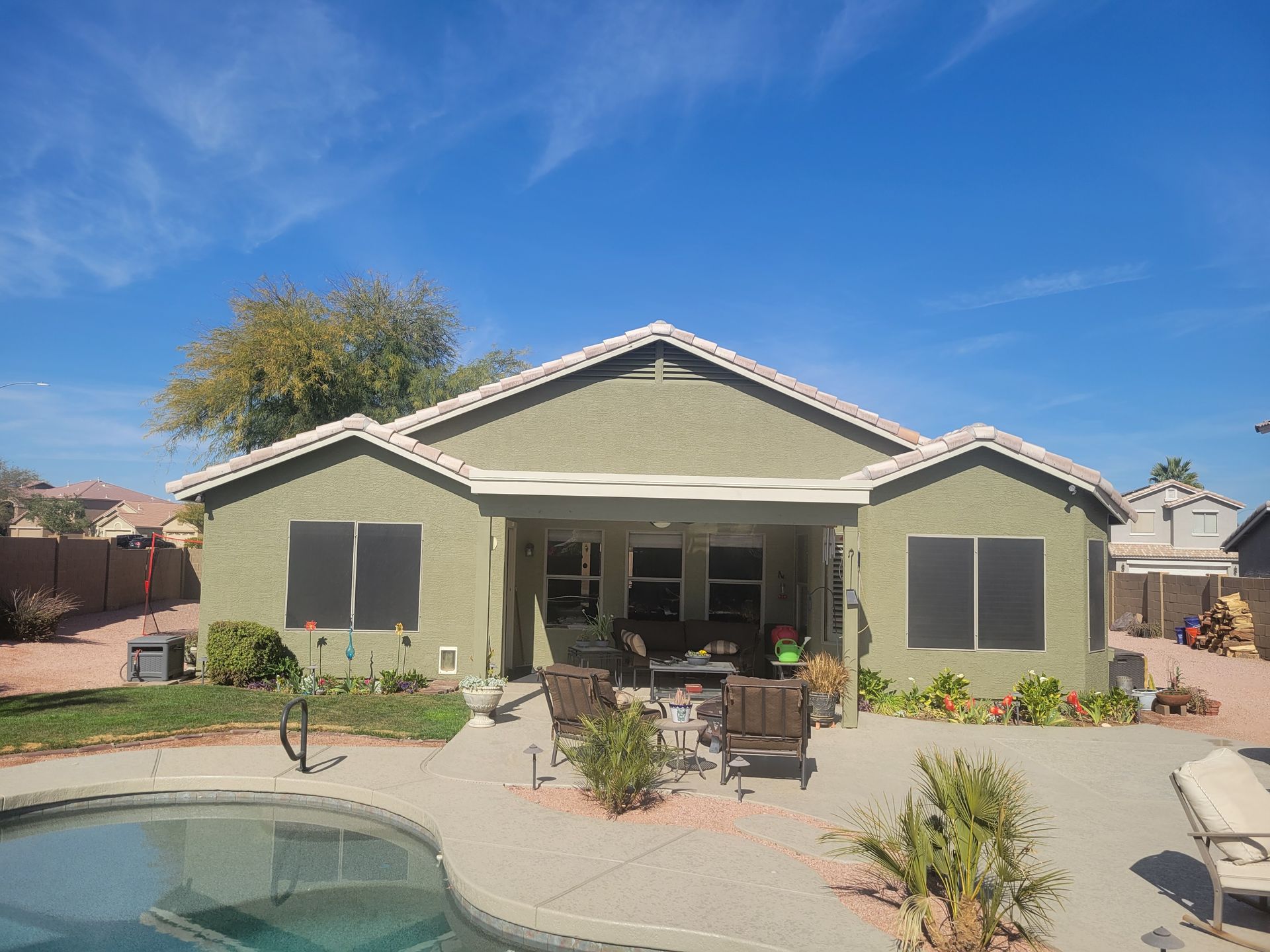 Backyard view of a green stucco house with a pool, sunny blue sky, and patio furniture.