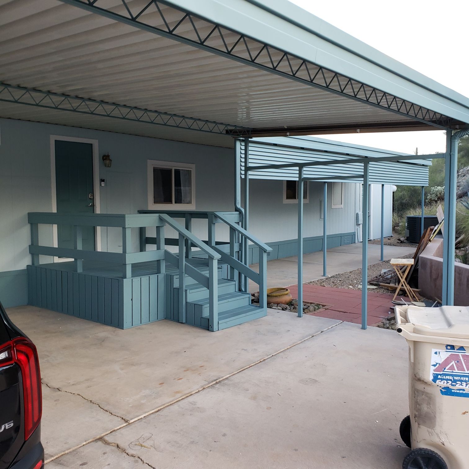 Blue mobile home with porch and awning, driveway, and trash can.
