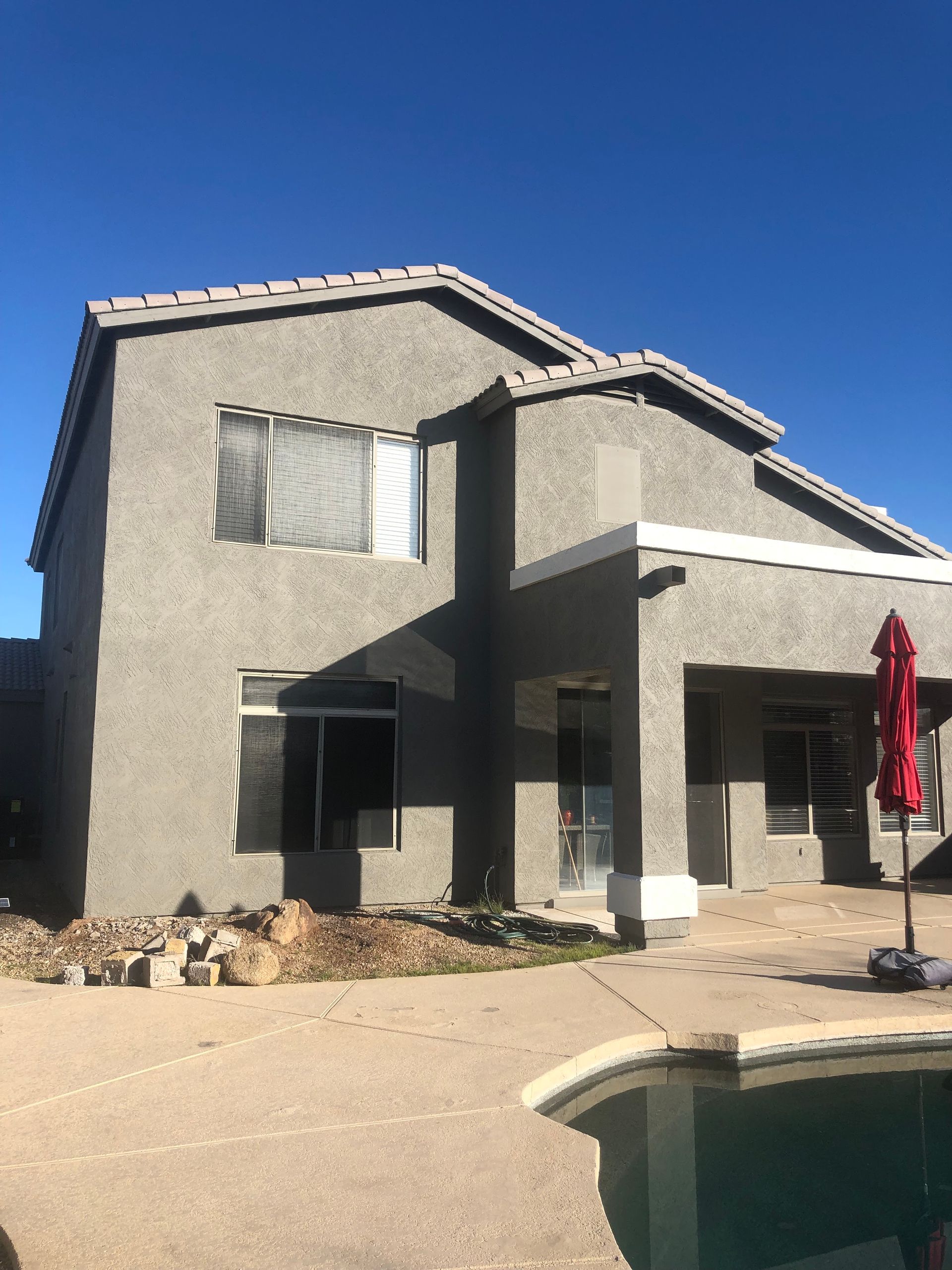 Two-story stucco house with a pool; clear, blue sky.
