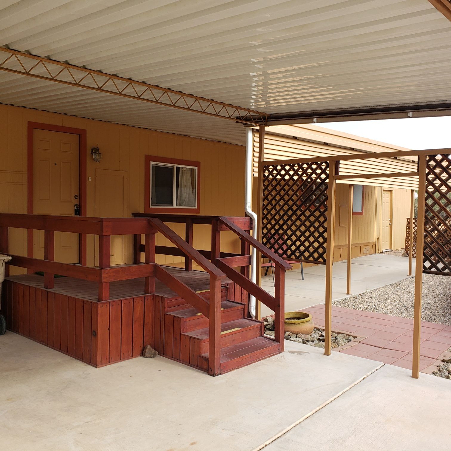 Exterior of a mobile home with a wooden deck and covered walkway.