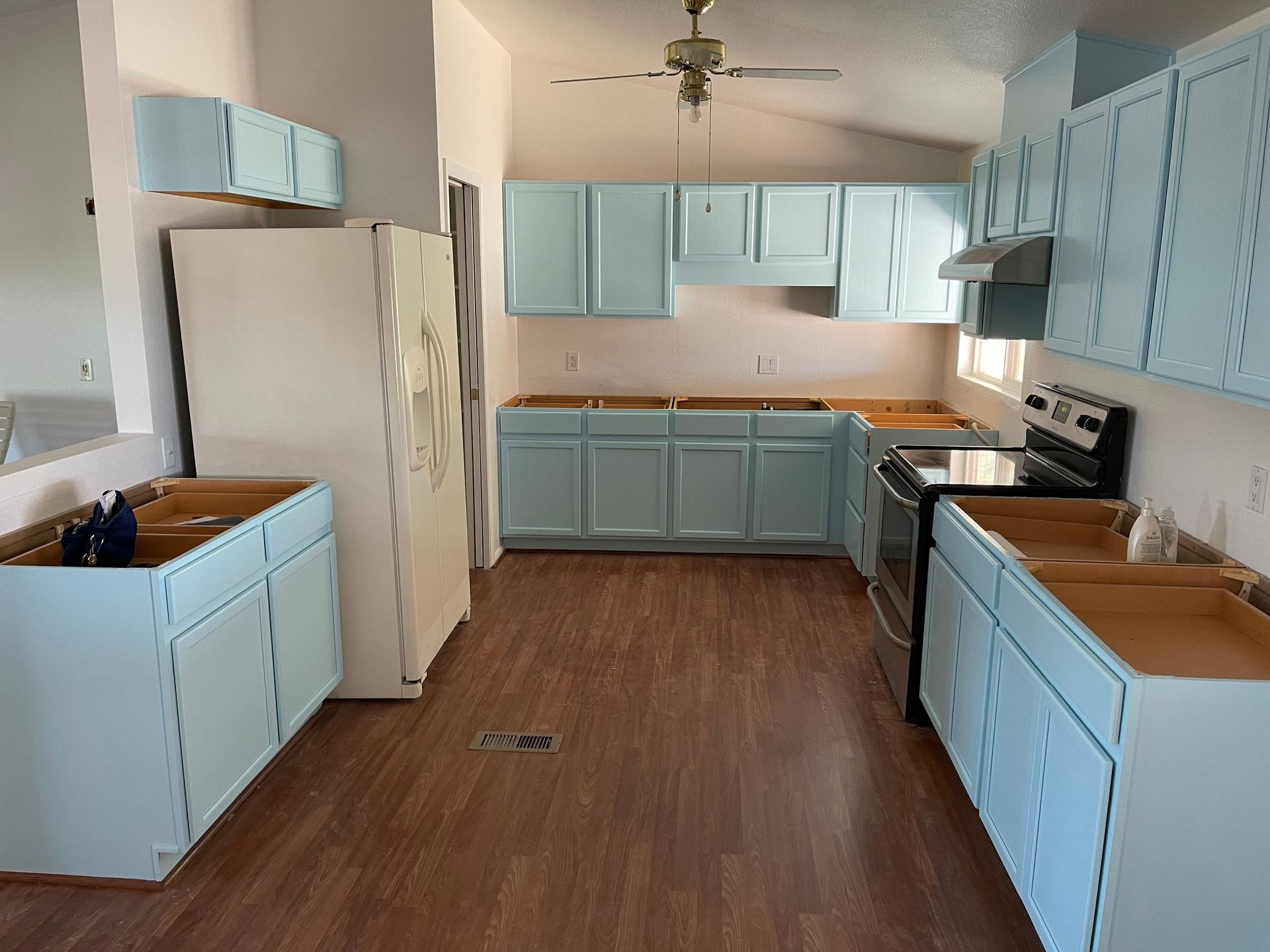 Kitchen with pale blue cabinets, wood floors, a white refrigerator, and a black stove.