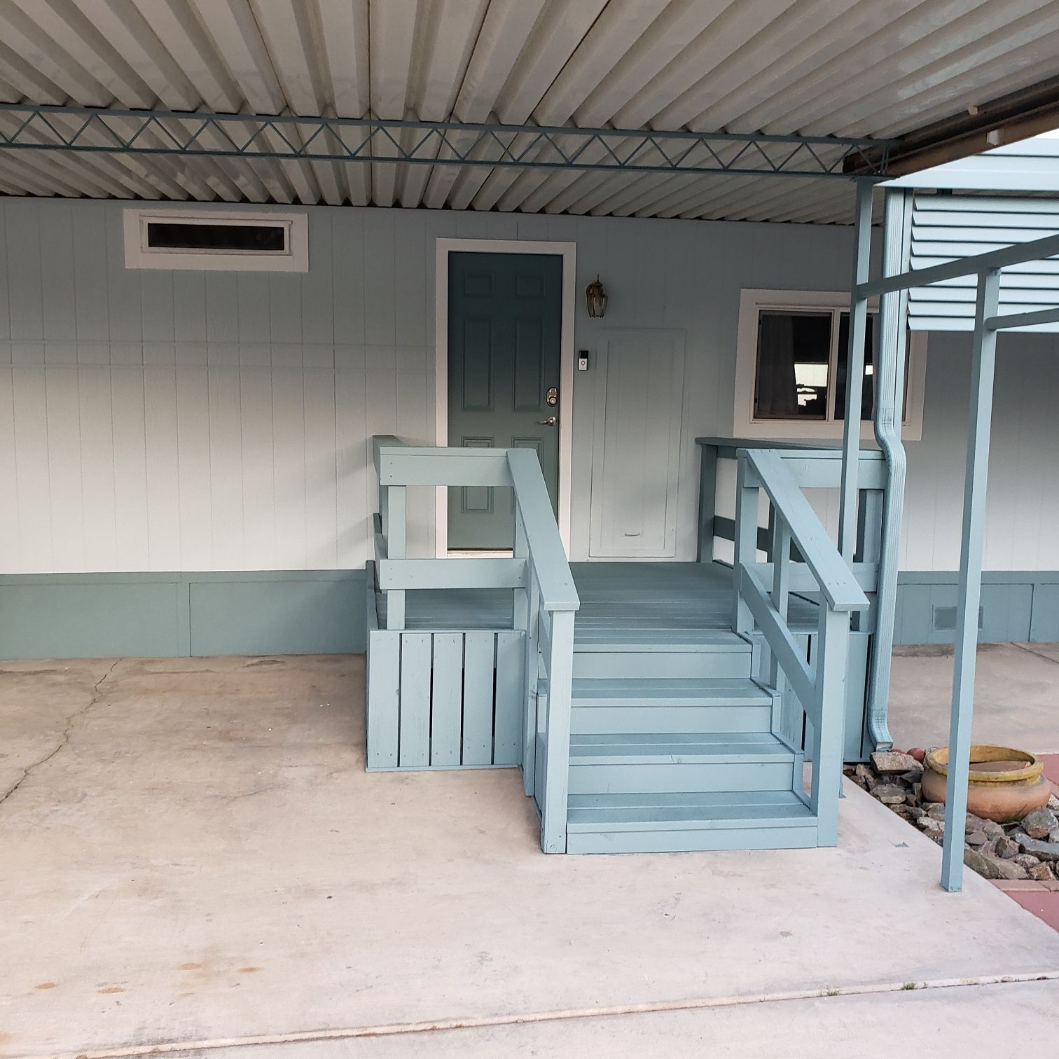 Blue-painted steps lead to a matching door and porch on a light blue house under a carport.
