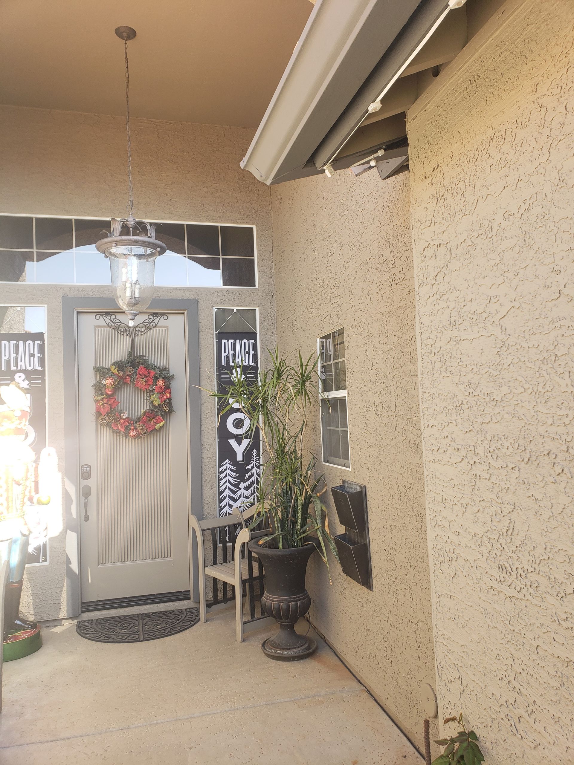 A festive porch with a decorated door, wreath, and potted plants.