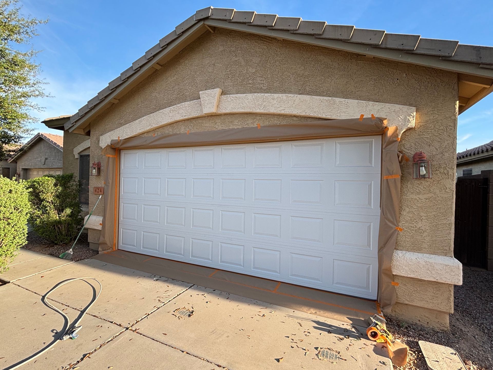 White garage door on a stucco house under a blue sky. Orange tape on trim.