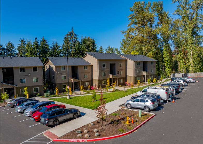 Harmona Heights Apartment community – exterior partial view of beige buildings in apartment community and parking lot.
