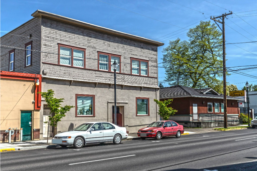 Armory Apartments in downtown Albany Oregon – gray building exterior with tree and neighboring building.