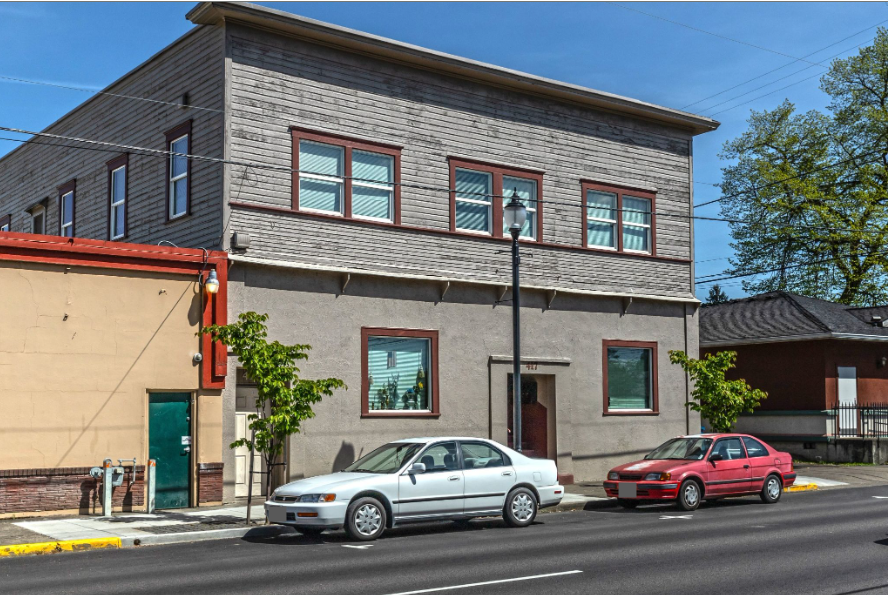 Armory Apartments in downtown Albany Oregon – gray building exterior with tree and neighboring buildings.