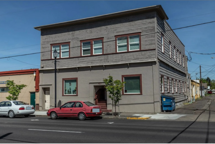 Armory Apartments in downtown Albany Oregon – gray building exterior with tree and alley.
