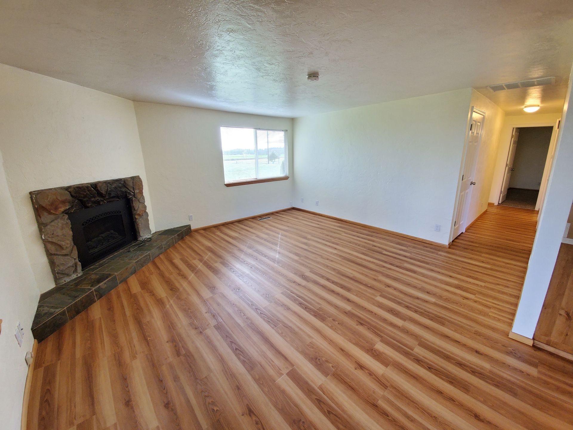 Amanda Lane Duplexes in Millersburg Oregon, three-bedroom two-bathroom – living room with fireplace, wood flores and window.