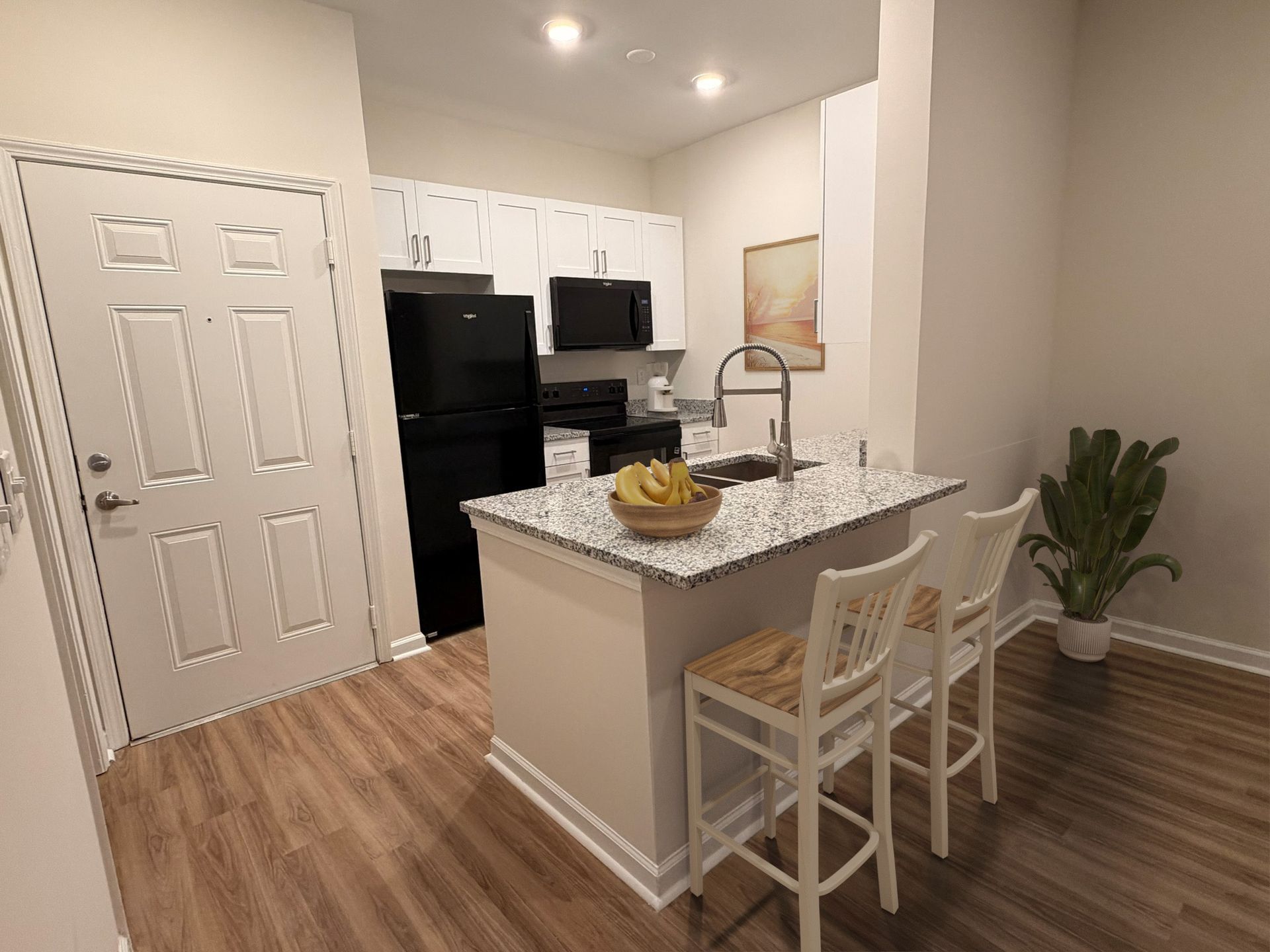 Kitchen area in an apartment with a granite island, white cabinets, and black appliances.