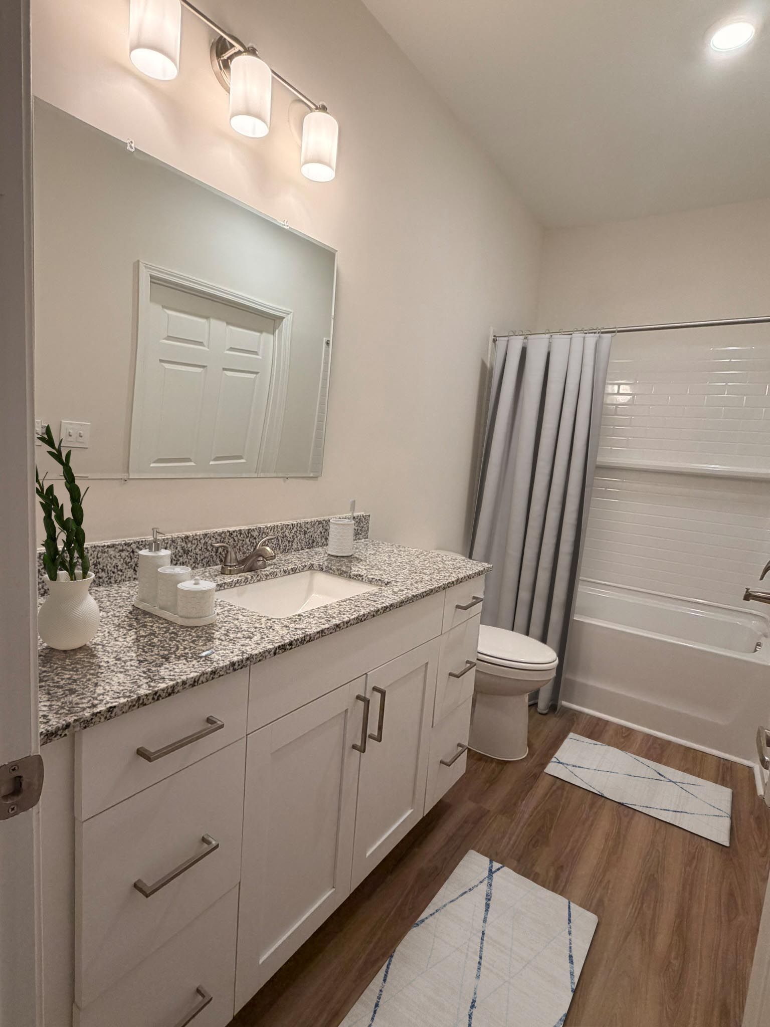 Bathroom vanity with granite countertop, sink, large mirror, toilet, tub/shower, and white cabinetry.