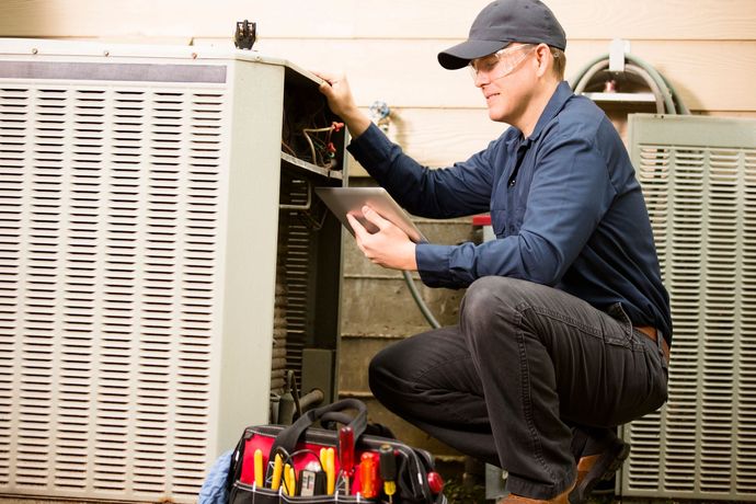 A man is working on an air conditioner while looking at a tablet.