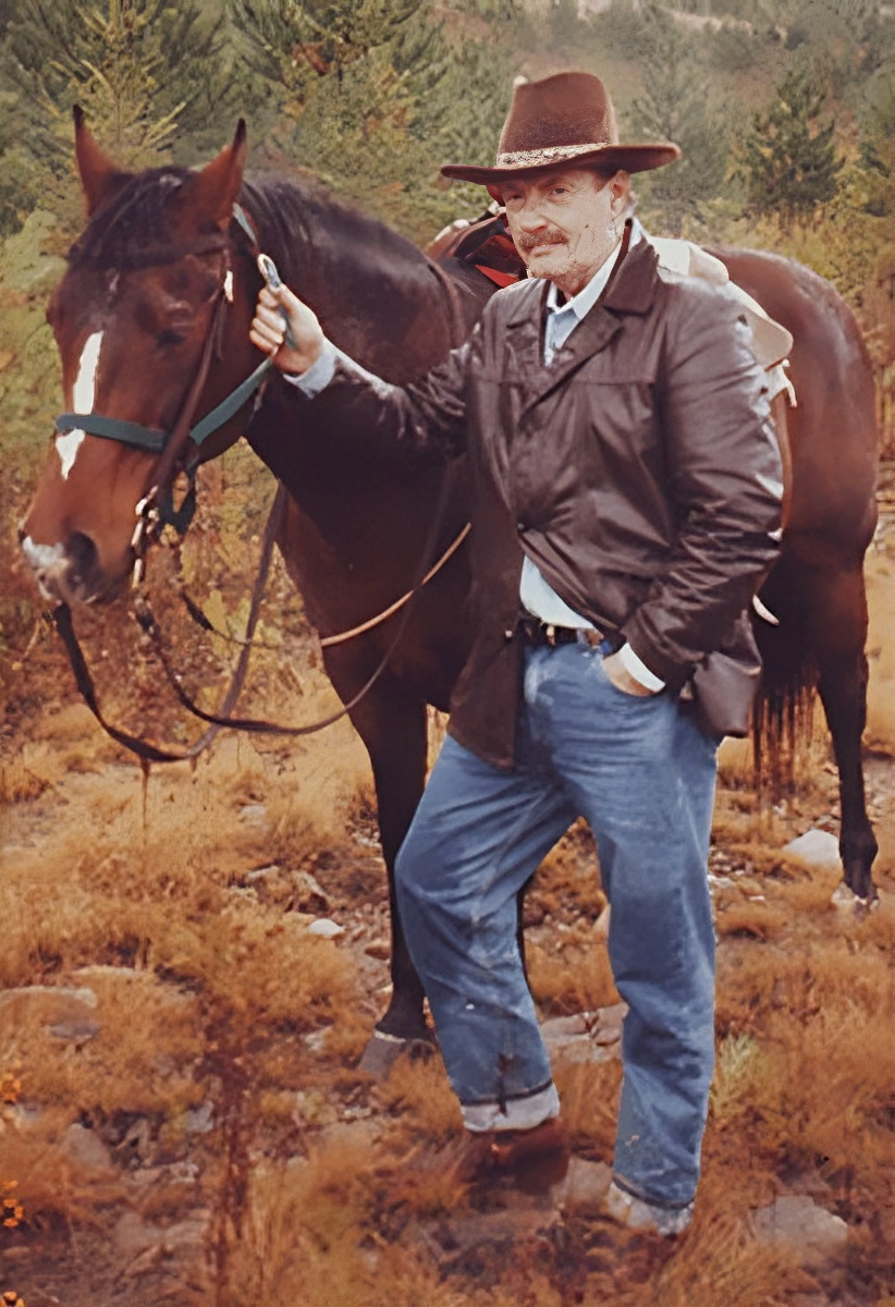 A man in a hat stands next to a brown horse