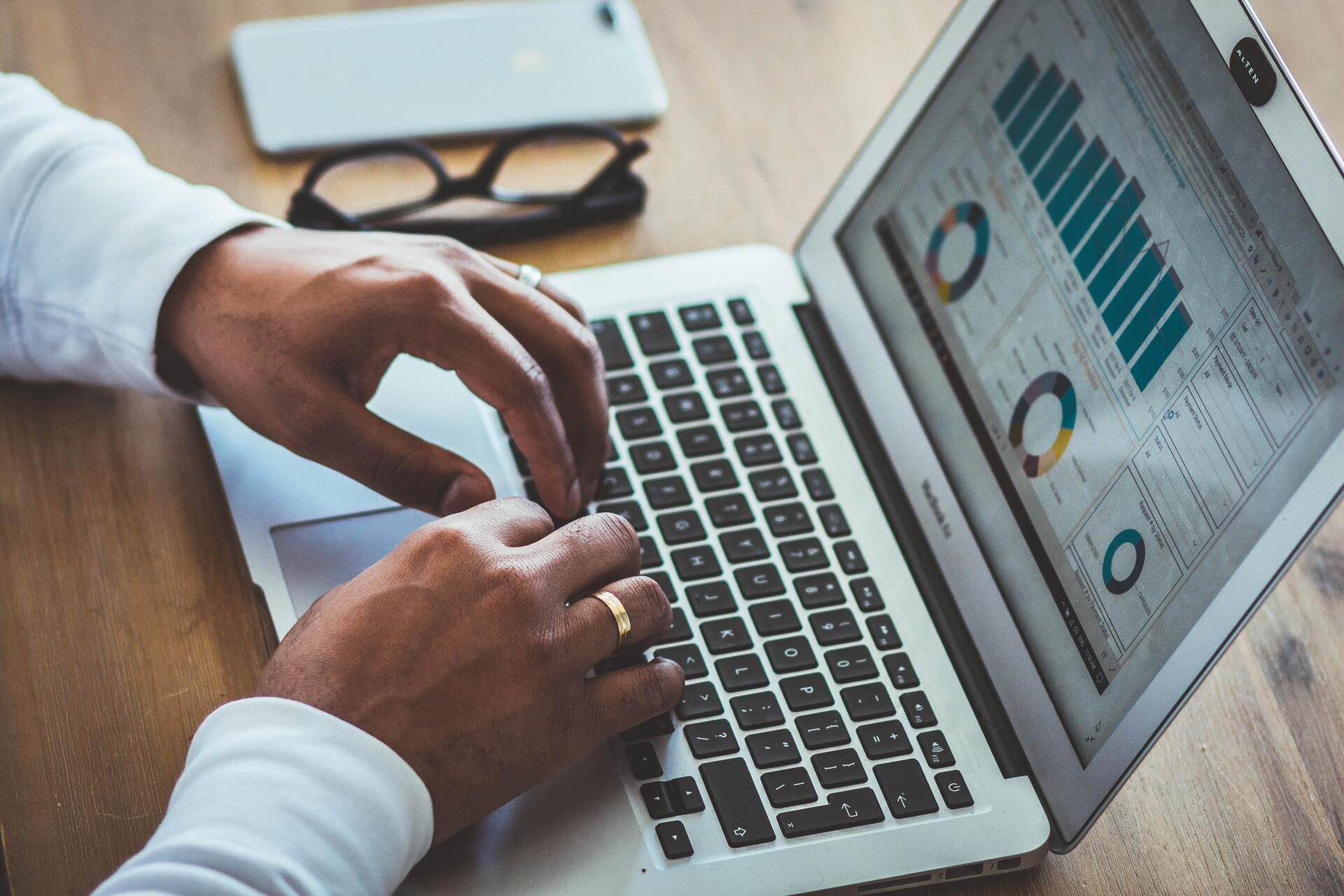 Person working on computer with phone and glasses on side looking at graphs charts business solutions