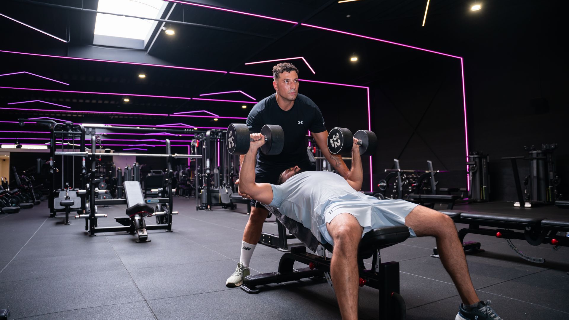 Interieur van een sportschool met rijen fitnessapparaten, donkere vloer en muren.