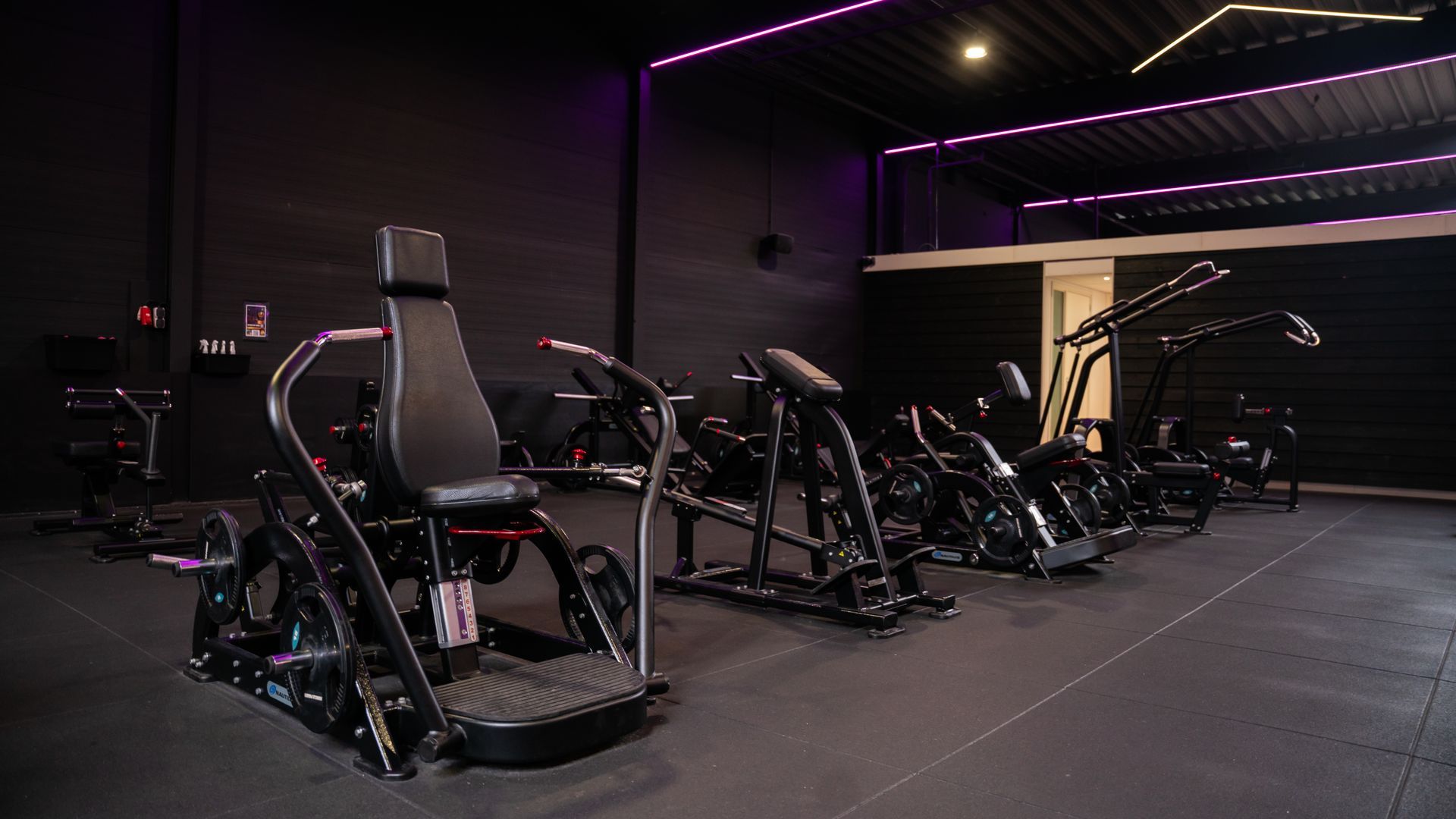 Een sportschool met schemerige verlichting, een groene kunstgrasbaan en fitnessapparatuur.