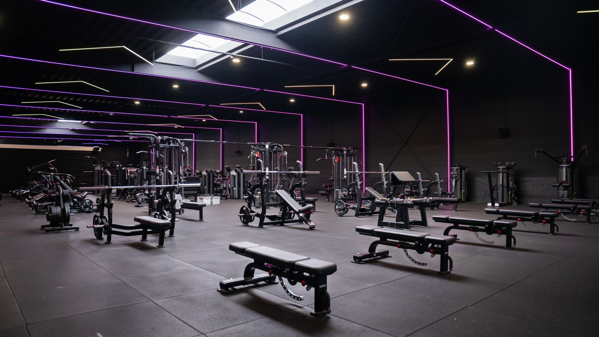 Interieur van een sportschool met donkere decoraties, fitnessapparaten en een persoon die de apparatuur gebruikt.