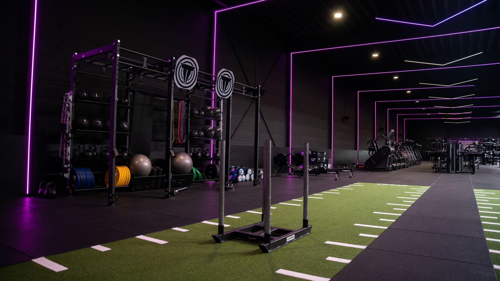 Mensen trainen in een sportschool, met een trainer. Drie mensen houden halters vast en oefenen op het kunstgras.