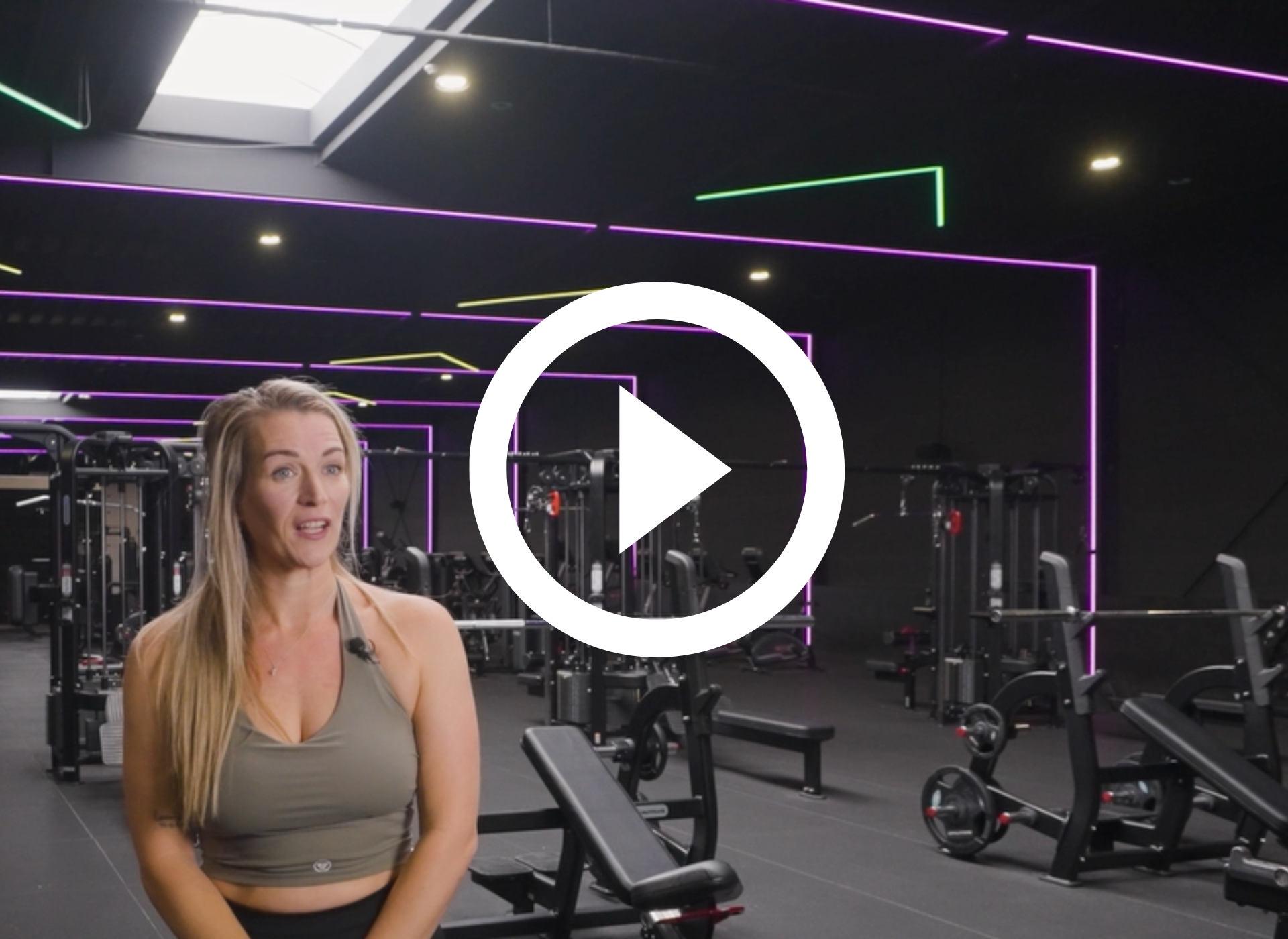 Man in de sportschool, lachend, met de afspeelknop erboven. Fitnessapparatuur op de achtergrond.