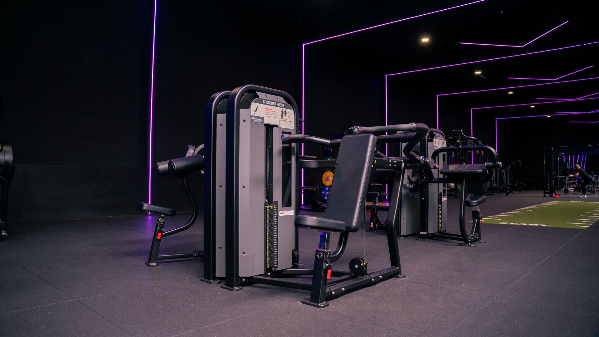 Interieur van een sportschool met fitnessapparaten en paarse sfeerverlichting.