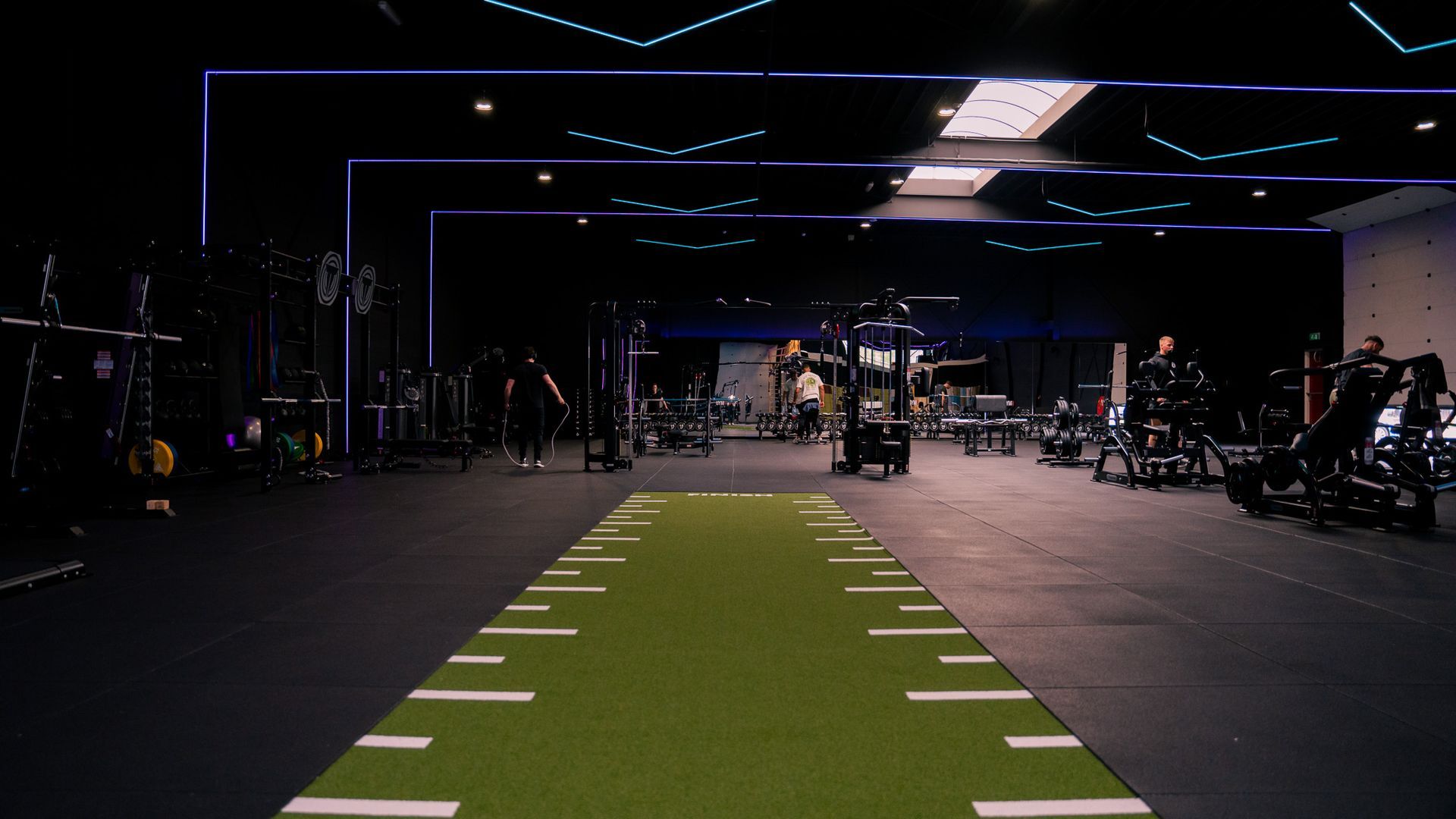 Donkere sportschool met groen gras, fitnessapparatuur en mensen die aan het sporten zijn.