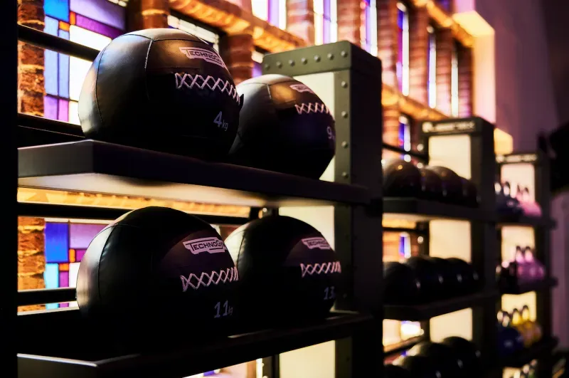 Zwarte medicijnballen op planken in een sportschool, vlak bij een glas-in-loodraam.