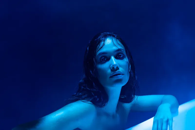 Een vrouw komt uit het blauwe licht, haar haar is nat en ze kijkt omhoog.