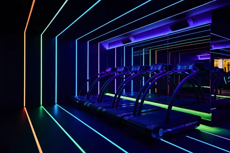 Neonverlichte sportschool met loopbanden. Kleurrijke lichtstrips omlijsten de apparaten en creëren een futuristische, energieke sfeer.