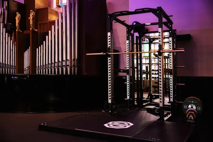 Gewichthefapparatuur in een kerk; donker metalen squatrek op een zwarte mat.