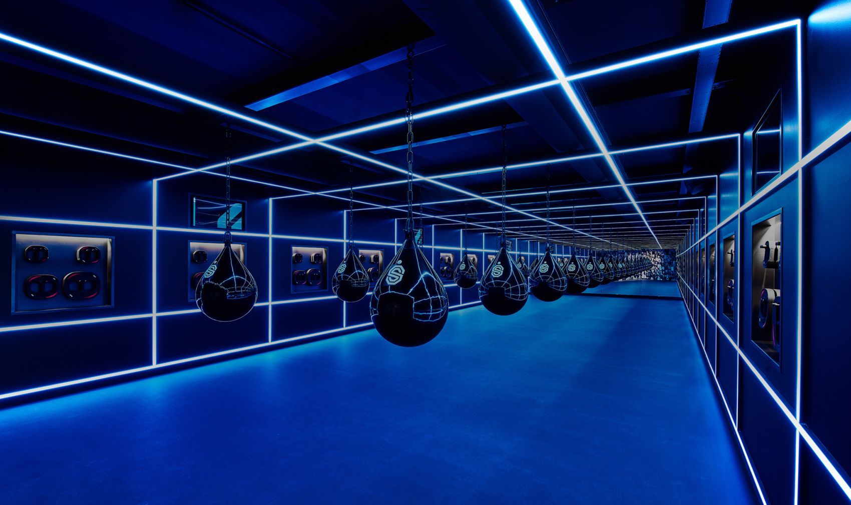 Blauw verlichte bokszaal met hangende bokszakken en ingelijste afbeeldingen aan de muren.