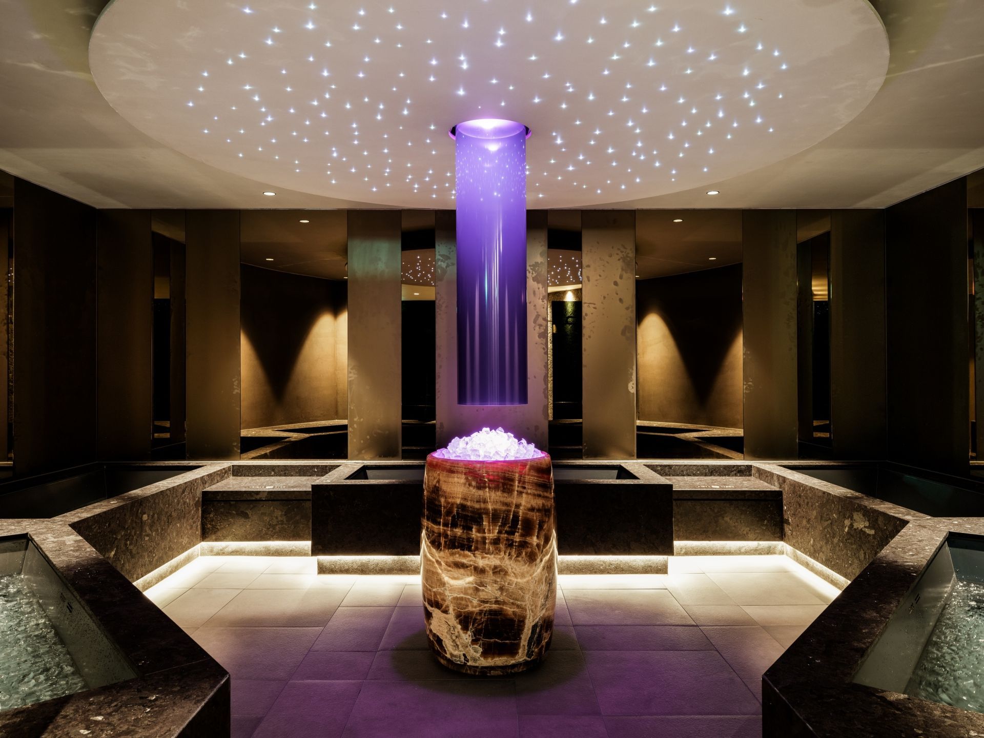 Spa-interieur met paarse lichtaccenten, sterrenplafond en stenen elementen.