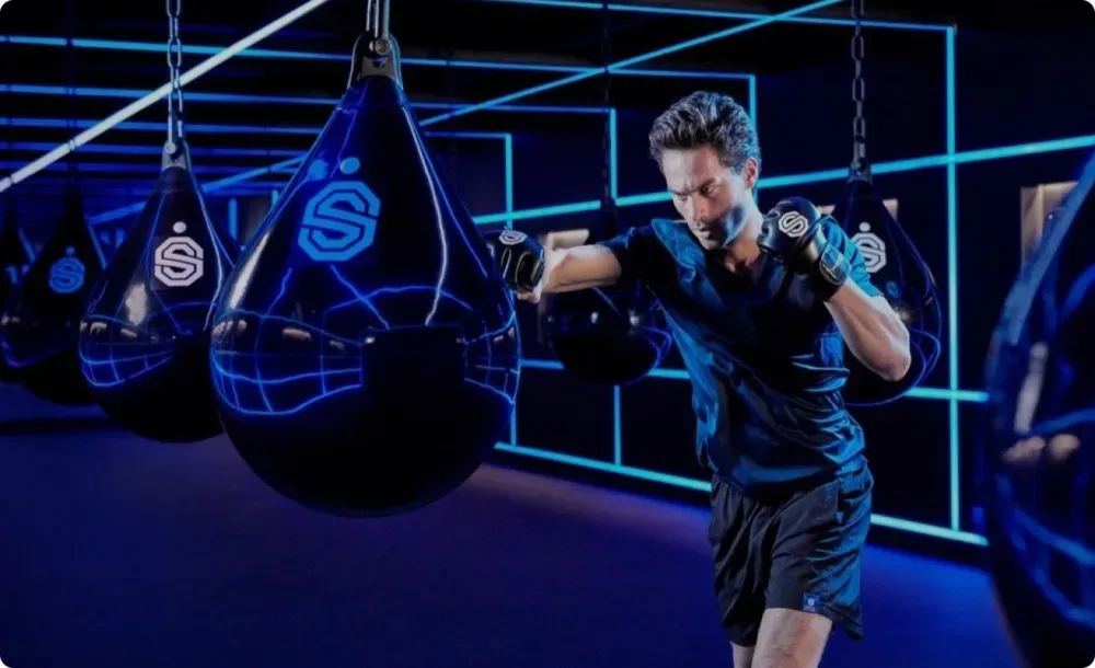 Man bokst met een druppelvormige boksbal in een neonverlichte sportschool.