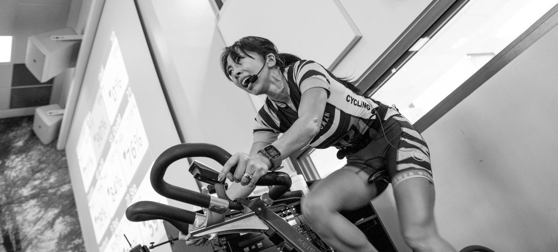 Vrouw op een hometrainer, die binnen aan het sporten is, ziet er geconcentreerd uit.