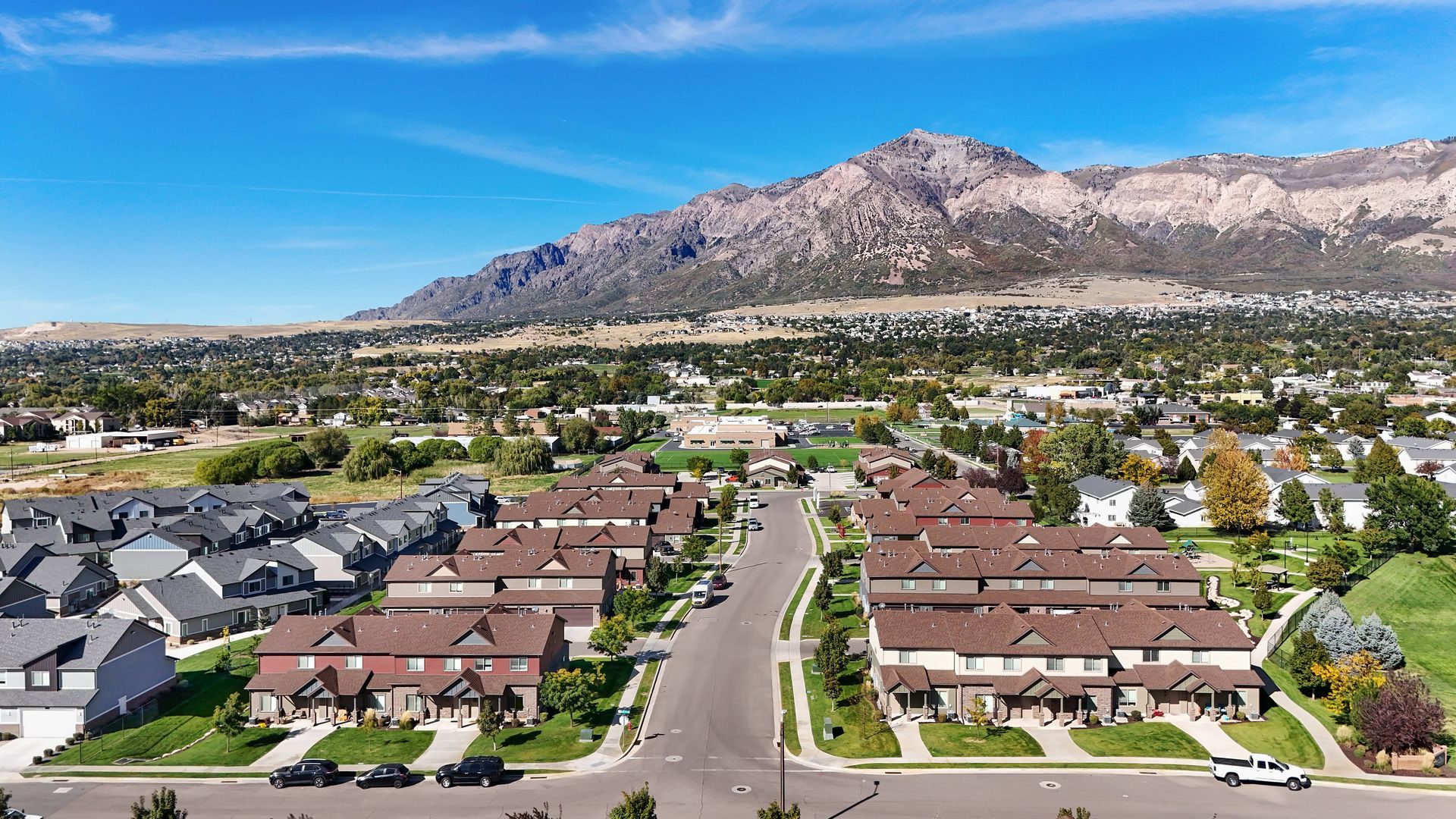 Suburban town with rows of brown-roofed homes, road leading to mountain under blue sky.