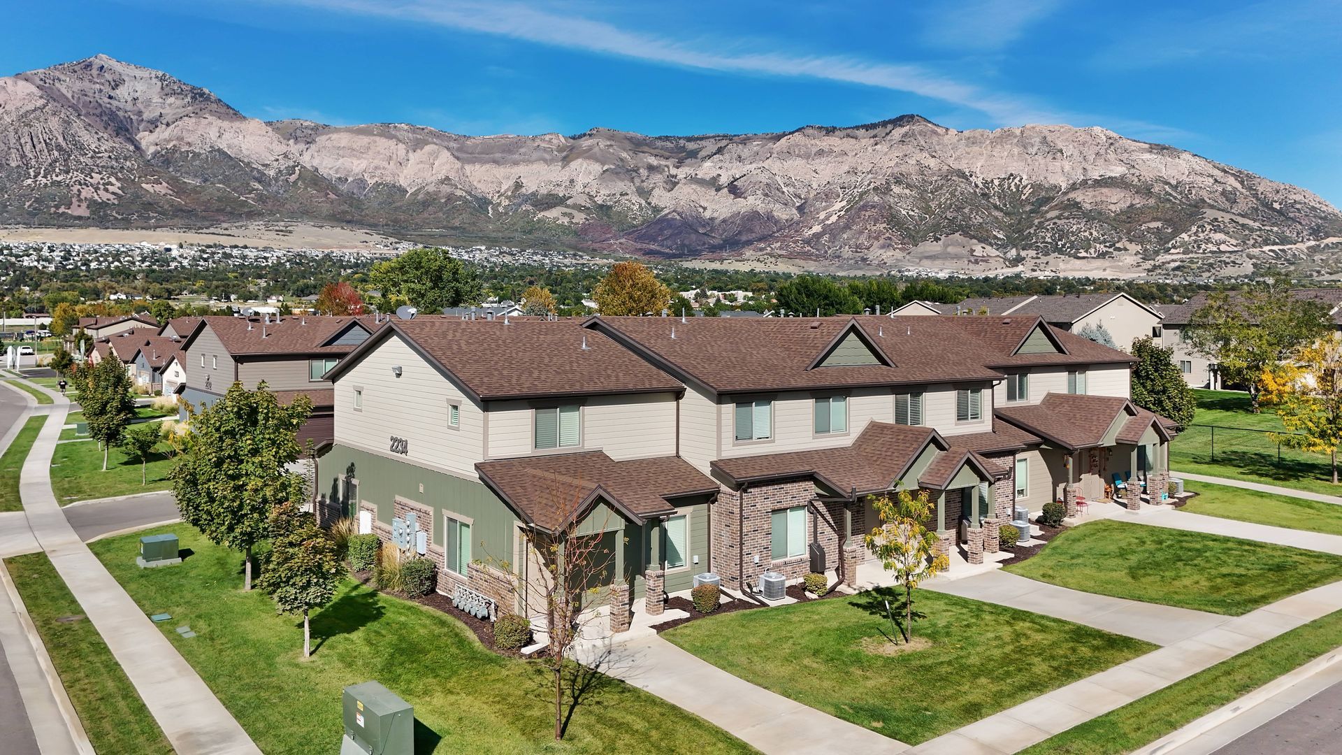 Row of townhouses with brown roofs and mountain backdrop on a sunny day.