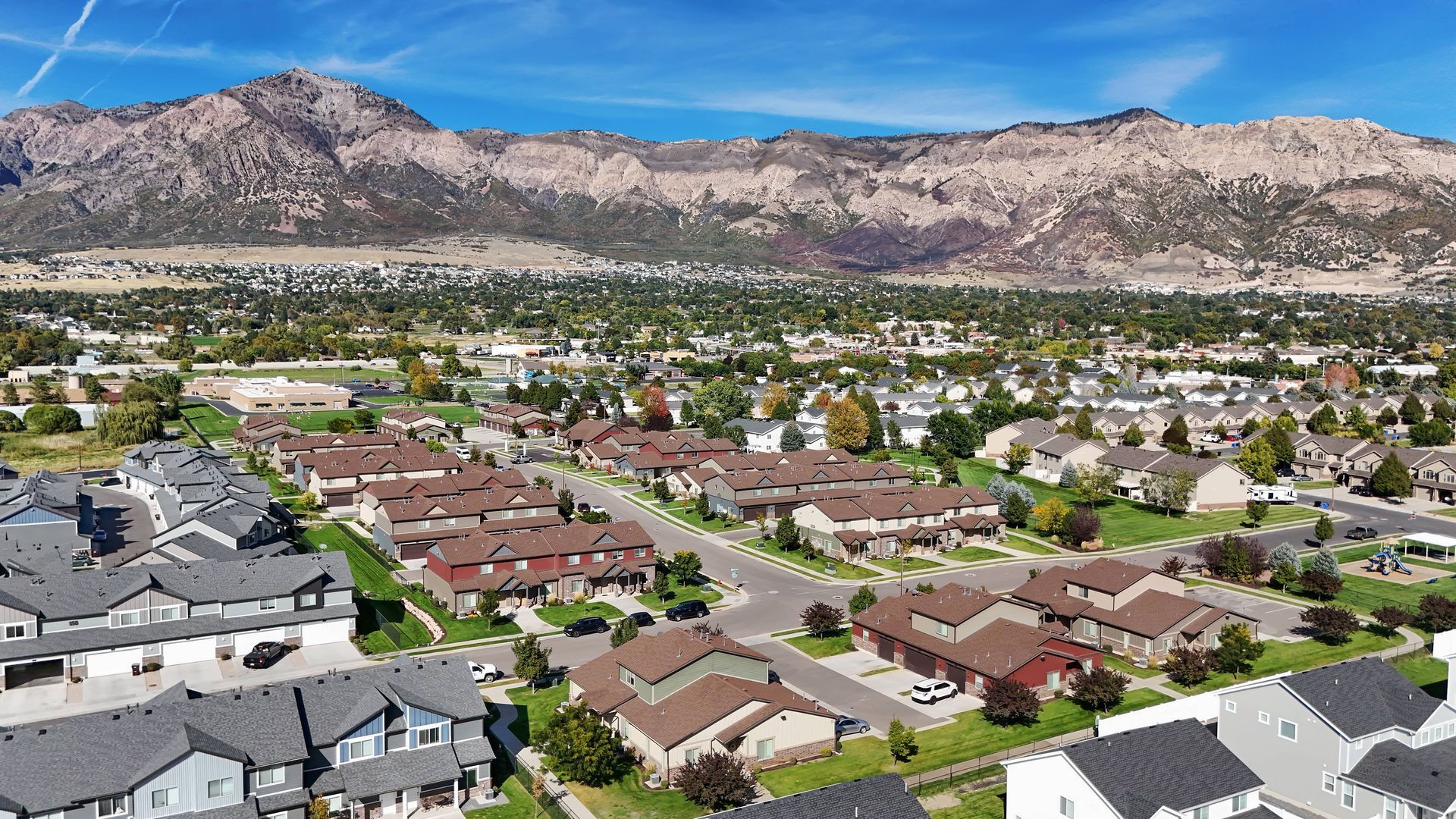 Aerial view of a suburban neighborhood with brown-roofed houses at the base of a mountain range under a clear blue sky.