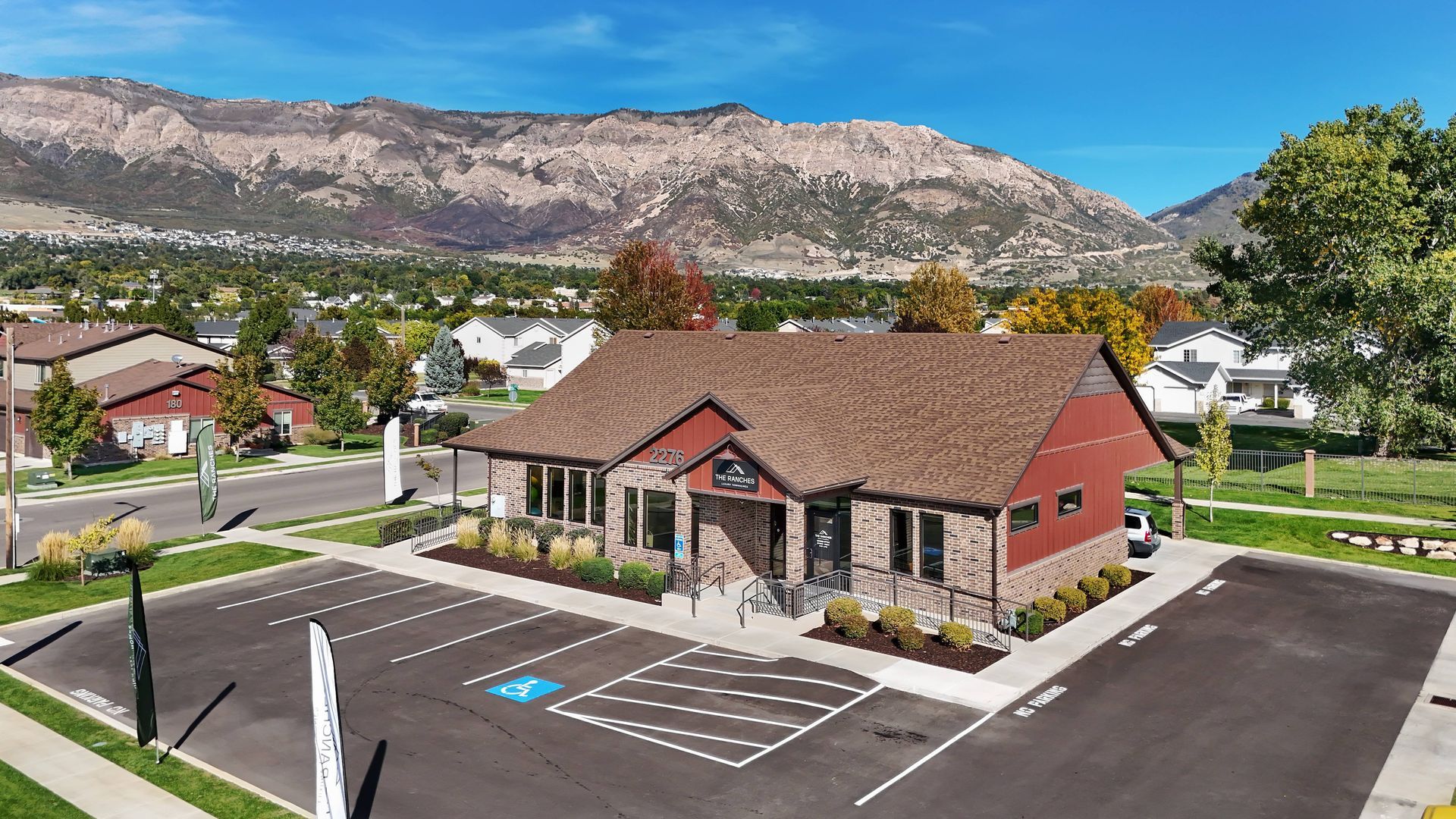 Office building with parking lot, mountains in the background, under a blue sky.
