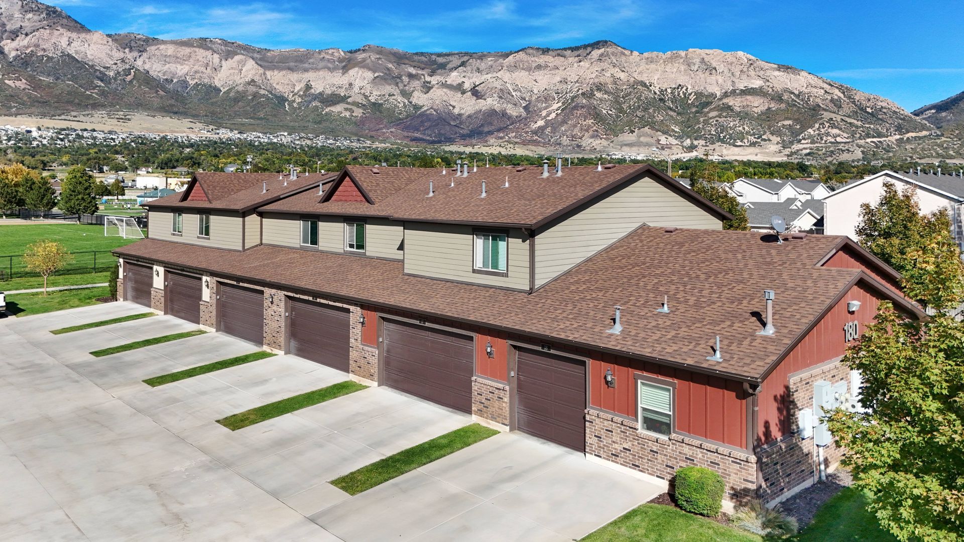 Row of townhouses with brown roofs and garage doors, red and stone facade, mountain backdrop.