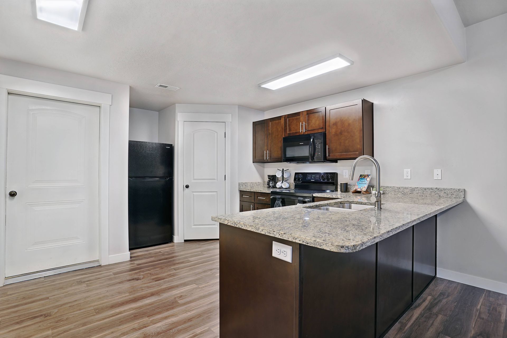 Kitchen with dark cabinets, granite countertops, island, black refrigerator, and wood flooring.