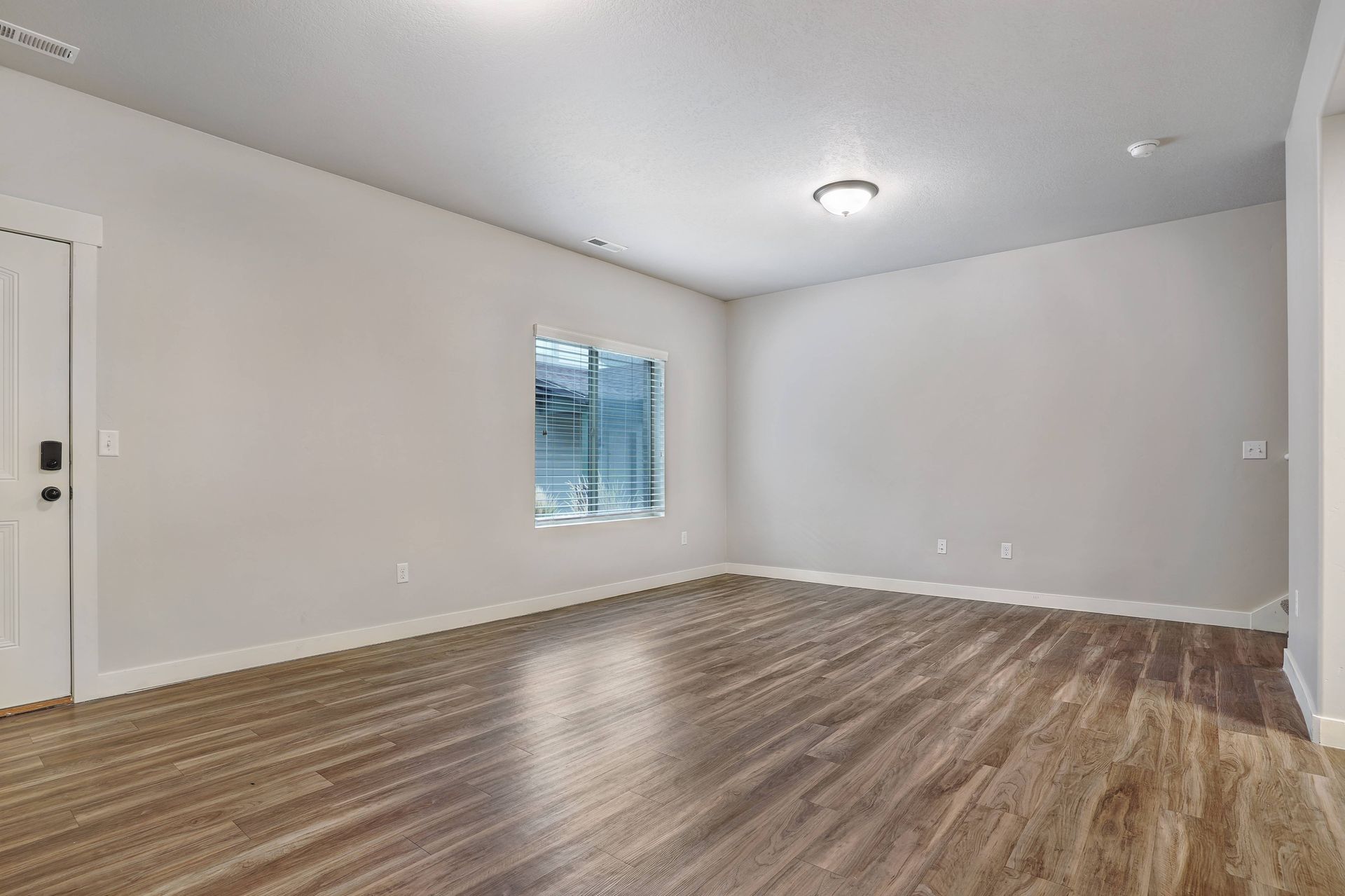 Empty room with wood-look floor, white walls, a window, and a door.