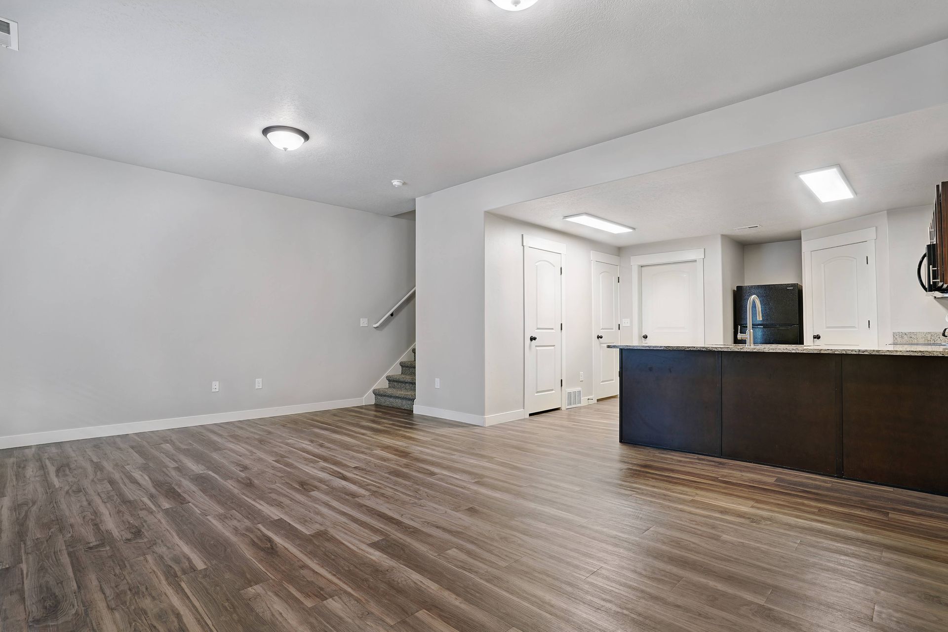 Empty living space with hardwood floors, stairs, and dark kitchen island.