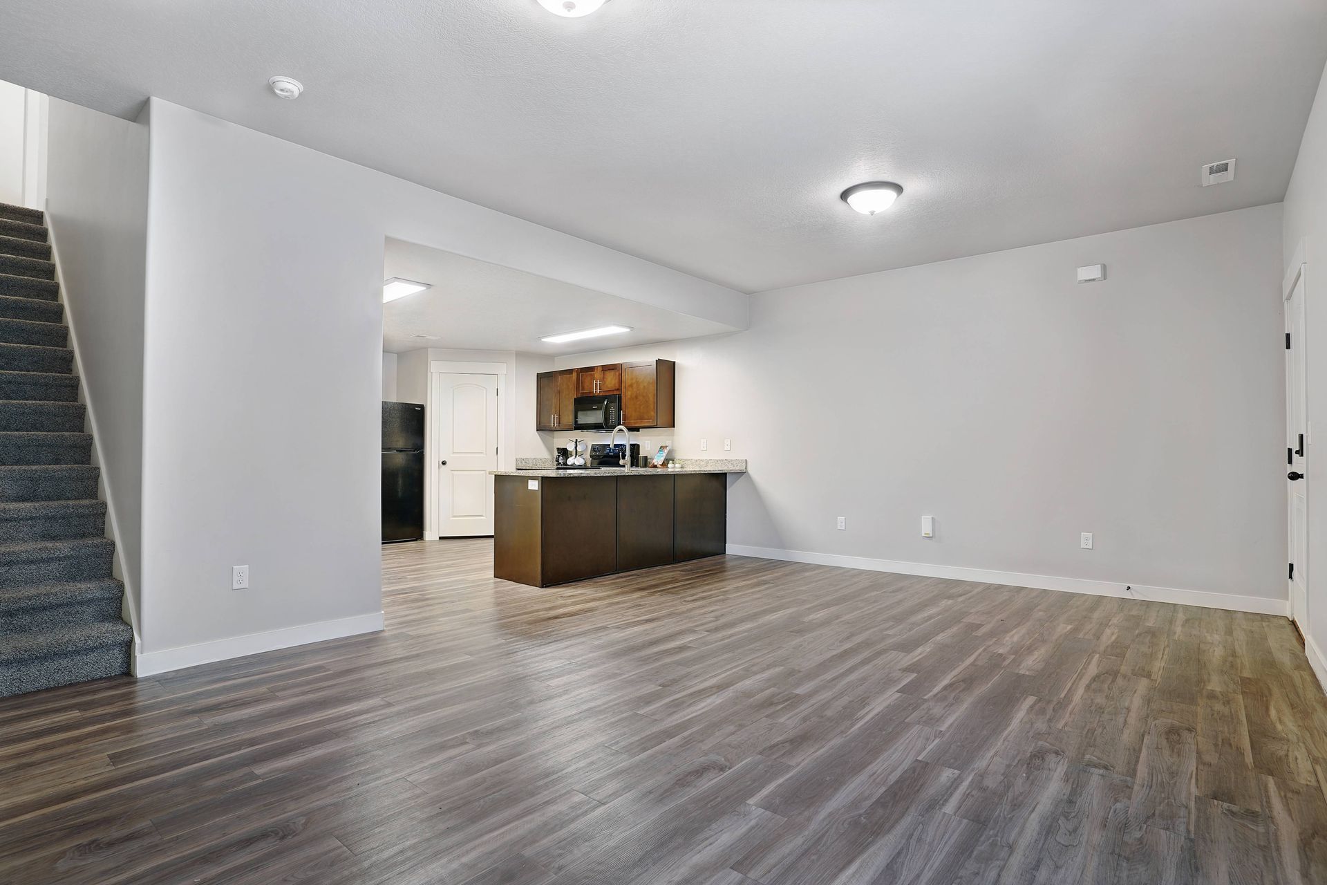 Spacious living area with staircase, open kitchen with island, and dark wood-look flooring.