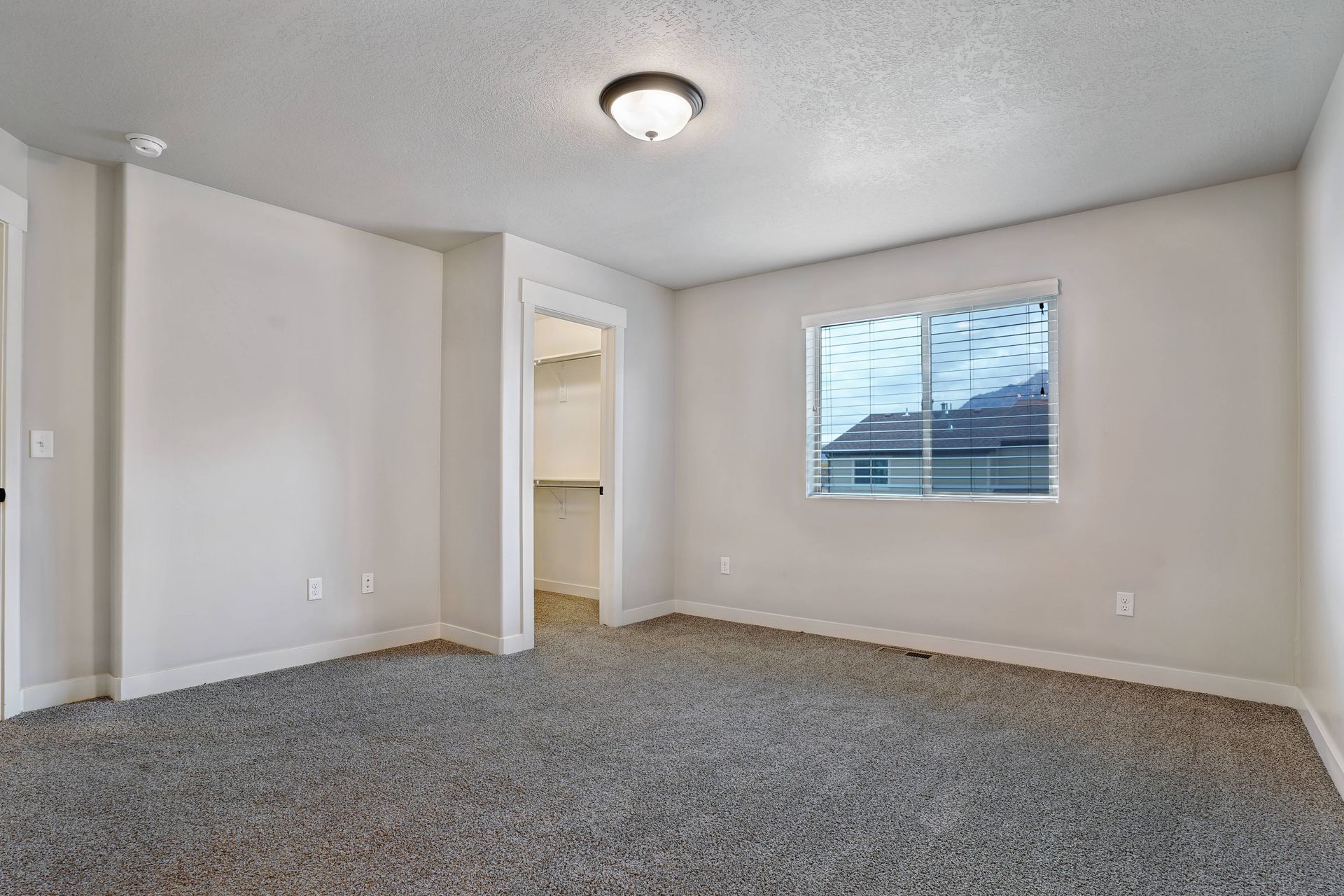 Empty bedroom with gray carpet, white walls, closet, and a window.