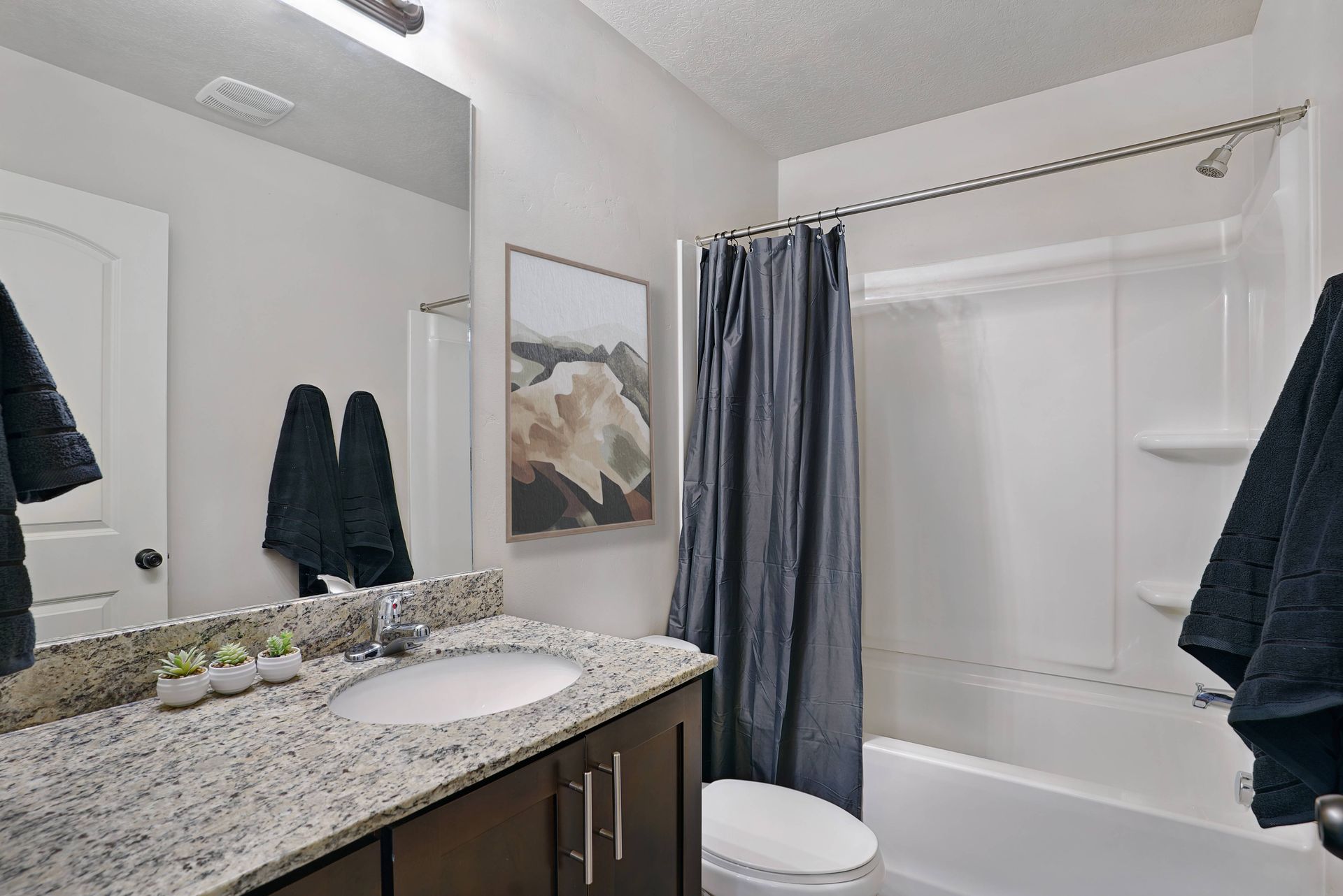Bathroom with granite countertop vanity, tub with shower curtain, black towels.