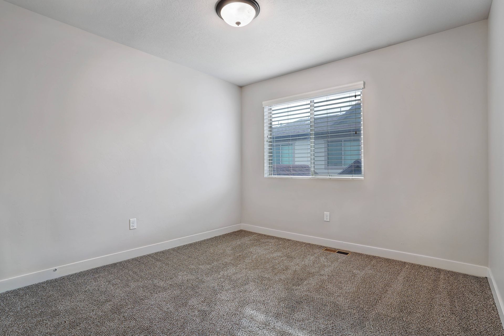 Empty bedroom with gray carpet, window with blinds, and a ceiling light.