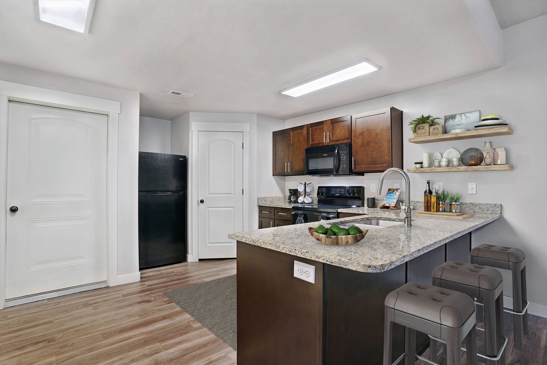 Kitchen with dark brown cabinets, granite countertop island, and stools. Black appliances and white doors.