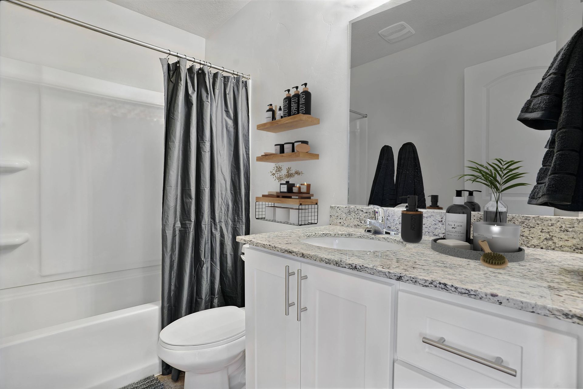 Bathroom with white cabinets, granite countertop, shower, and decorative shelves.