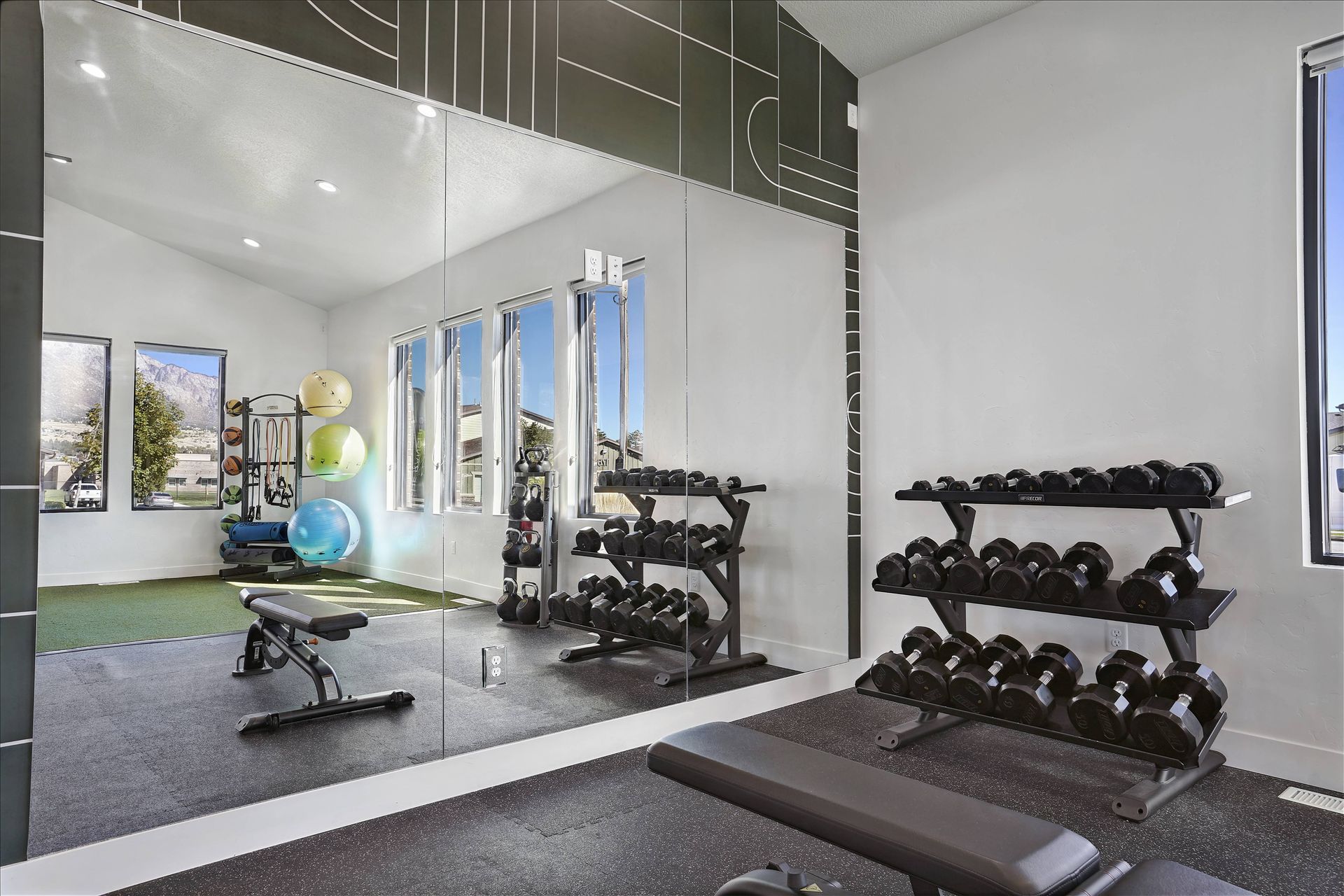 Home gym with weight racks, bench, and mirror wall, bright room with a view.